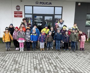 Na zdjęciu widać na tle budynku Komendy Powiatowej Policji w Wadowicach stoi grupa dzieci przodem. Po prawej i po lewej stronie kobieta w stroju cywilnym.