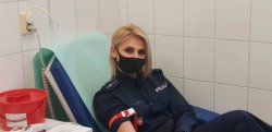 Umundurowana policjantka z maseczką założoną na usta i nos, siedząca na szpitalnym łóżku, oddająca krew.