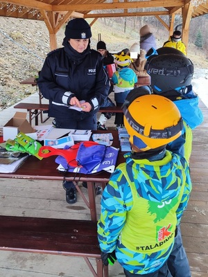 Umundurowana policjantka i stojące obok dzieci w strojach narciarskich.