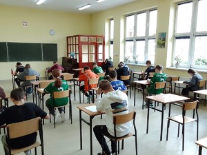 Uczniowie siedzący na krzesłach przy stolikach. osoby siedzą w klasie, są tyłem.