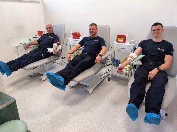 Trzech umundurowanych policjantów siedzących na łóżkach szpitalnych, którzy oddają krew