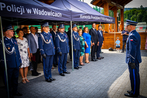 Po prawej stronie stoi Komendant Powiatowy Policji w Wadowicach stojący obok namiotu w którym stoi czterech policjantów i zaproszeni goście.