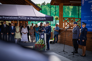 Po prawej stronie stoi policjantka i policjant, po lewej przemawiający Zastępca Komendanta Wojewódzkiego Policji w Krakowie. W tle pod namiotem zaproszeni goście.