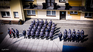 Zdjęcie z lotu ptaka, poukładani w szeregach policjanci w strojach galowych  oraz poczet sztandarowy.