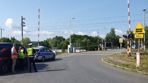 Na zdjęciu przejazd kolejowy, po lewej stronie oznakowany radiowóz i samochód Straży Ochrony Kolei, obok stoi policjant ruchu drogowego, funkcjonariusz Straży Ochrony Kolei oraz przedstawiciel Polskich Kolei.