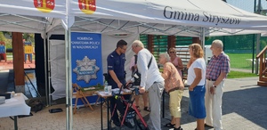 grupa seniorów przy stoisku firmowym KPP Wadowice, przy stoisku stoi umundurowany policjant, który prezentuje stoisko