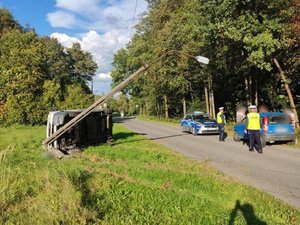 Miejsce zdarzenia drogowego, poza droga przewrócony na bok samochód osobowy oparty o słup energetyczny, w pobliżu policjanci i radiowóz oznakowany.