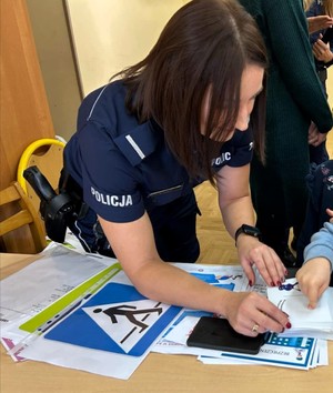 Umundurowana policjantka, która odbija linie papilarne dziecku. na stoliku poukładane są różne ulotki.