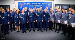 Na zdjęciu grupa umundurowanych policjantów i policjantek stojących na tle policyjnego baneru z napisem Komenda Powiatowa Policji w Wadowicach.