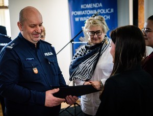 Umundurowany policjant wręczający podziękowania dwóm młodym dziewczynom. W tle dwie kobiety.