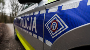 Boczna strona radiowozu. Na niebieskim tle biały napis Policja oraz logo ruchu drogowego.