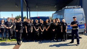 Uczniowie klasy o profilu policyjnym, w czarnych mundurach. Po prawej stronie policjant ruchu drogowego oraz oznakowany radiowóx.