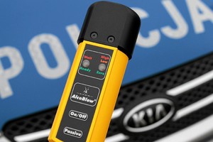 AlcoBlow alkomat na tle maski radiowozu koloru niebieskiego z białym napisem Policja