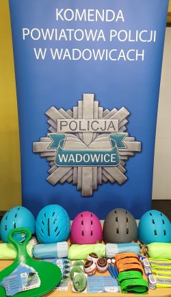 Na tle niebieskiego baneru, na którym widnieje biały napis Komenda Powiatowa Policji w Wadowicach oraz odznaka policyjna koloru szarego z napisem Policja Wadowice, poukładane nagrody konkursowe.