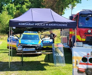 Namiot z napisem Komisariat Policji w Andrychowie pod którym na stoliku poukładany jest sprzęt policyjny i ulotki. W tle radiowóz i wóz strażacki.