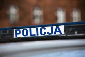 Na białym tle niebieski napis Policja. Po prawej i po lewej stronie niebieskie światła.