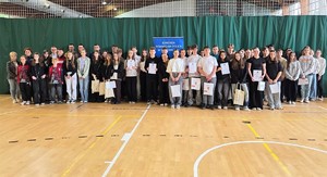 Na zdjęciu grupa osób stojących przodem. Niektóre osoby trzymają w rękach dyplomy i torby papierowe.