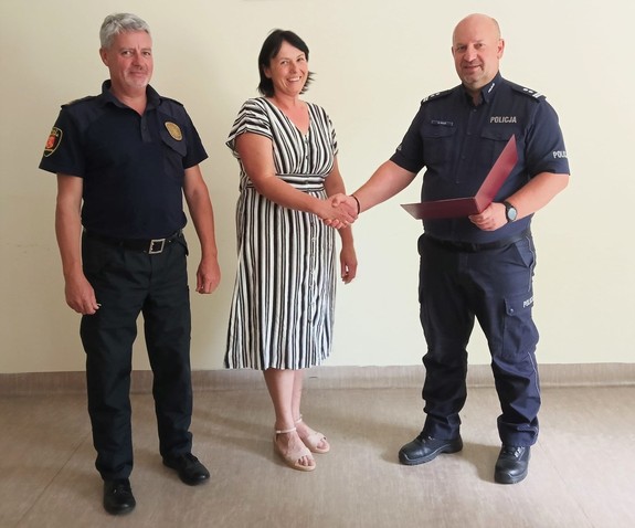 Na zdjęciu Komendant Straży Miejskiej w Andrychowie, kobieta w sukience ora Komendant Komisariatu Policji w Andrychowie. Policjant gratuluje kobiecie i wręcza jej list gratulacyjny.