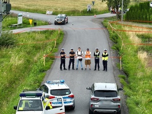 Na zdjęciu z lotu ptaka widać w otaśmowanej części drogi czterech policjantów i dwóch mężczyzn w stroju cywilnym. Na dole zdjęcia radiowóz i dwa samochody. W tle samochód rajdowy na trasie.