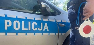 Boczna strona radiowóz i policjant trzymający tarcze sygnalizacyjną
