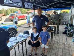 na stoisku policyjnym chłopiec z dziewczynką pozują do zdjecia z policjantem