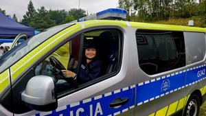 W radiowozie siedzi dziewczynka ubrana w elementy umundurowania policyjnego.