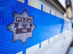 Boczna strona radiowozu. Na niebieskim tle  odznaka policyjna z napisem Policja 112