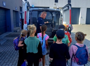 Policjant, który otwiera radiowóz. Przed nimi grupa dzieci.