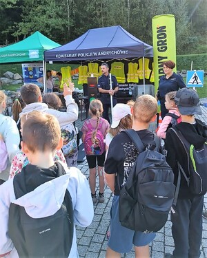 Policjant i policjantka, a przed nimi grupa dzieci. W tle namioty.