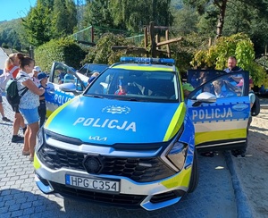 Oznakowany radiowóz i grupa dzieci go oglądających. Po prawej policjant.