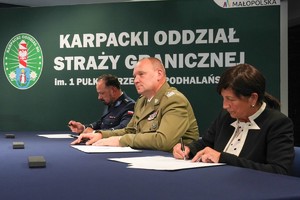 Przy stole siedzi dwóch umundurowanych mężczyzn i kobieta w stroju cywilnym