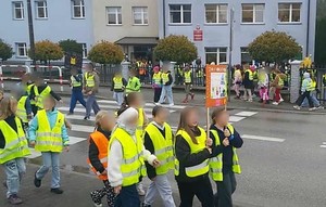Dzieci w kamizelkach odblaskowych przechodzące przez przejście dla pieszych przed szkołą