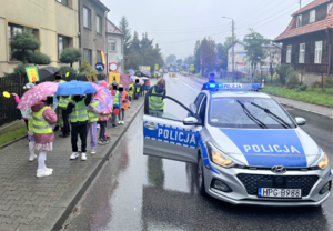 Na chodniku dzieci w kamizelkach odblaskowych, na drodze oznakowany radiowóz