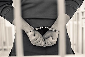 Mężczyzna z kajdankami założonymi na ręce trzymane z tyłu, stojący za kratami