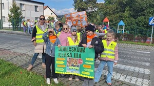 Grupa dzieci w kamizelkach odblaskowych trzymające  transparenty.