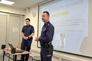 Na zdjęciu widać dwóch umundurowanych policjantów i wyświetlana w tle prezentację.
