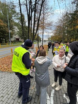 Policjant w kamizelce odblaskowej i grupa osób.