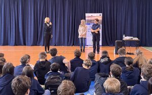 Dwie kobiety i policjantka, przed nimi grupa siedzących dzieci.