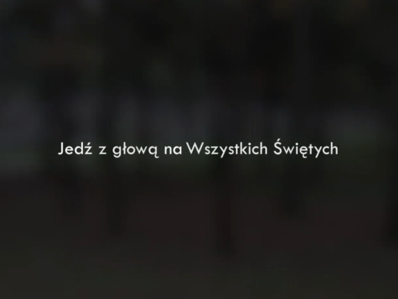 Na czarnym tle biały napis  Jedź z głową na Wszystkich Świętych
