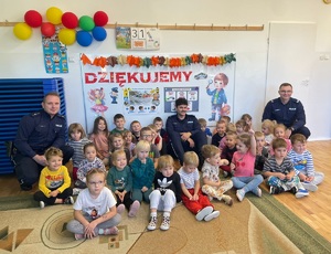 Grupa przedszkolaków siedzących na podłodze, a wśród nich trzech policjantów