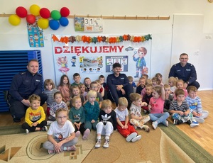 Grupa przedszkolaków siedzących na podłodze, a wśród nich trzech policjantów