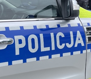 Boczna strona radiowozu. Na niebieskim tle biały napis Policja