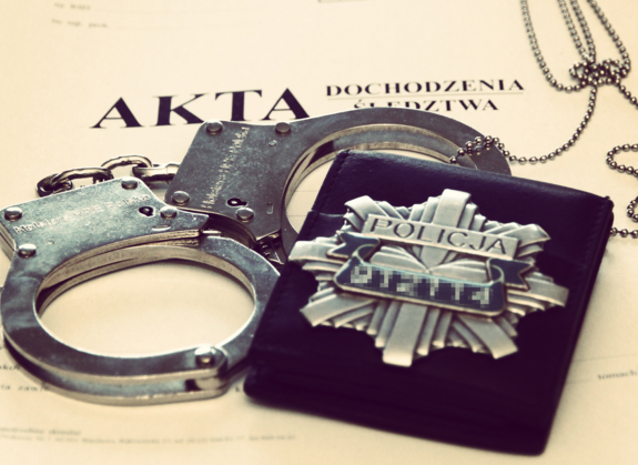 Na aktach sprawy policyjne kajdanki i odznaka policyjna