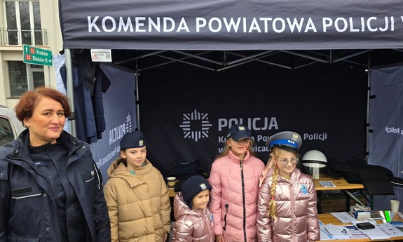 Policjantka i cztery dziewczynki, które mają założone policyjne czapki, W tle policyjny namiot