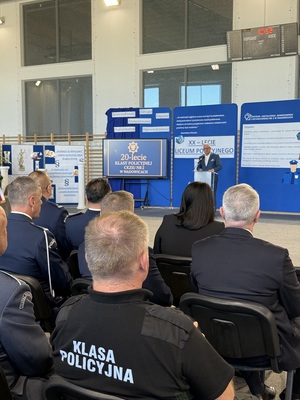 Starosta przemawiający z mównicy, przed nim osoby siedzące na krzesłach