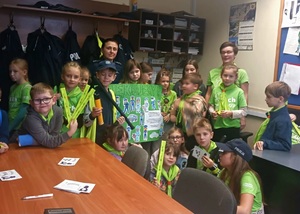 Grupa dzieci z odblaskami i plakatem oraz policjantka.