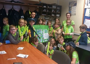 Grupa dzieci z odblaskami i plakatem oraz policjantka.