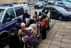 Przy radiowozie grupa dzieci i policjantka. W tle samochody.