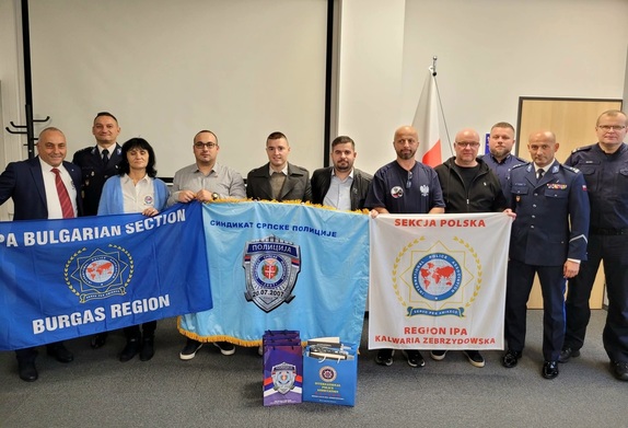Na zdjęciu mężczyźni w strojach cywilnych, umundurowani policjanci oraz kobieta. W rękach trzymają flagi.