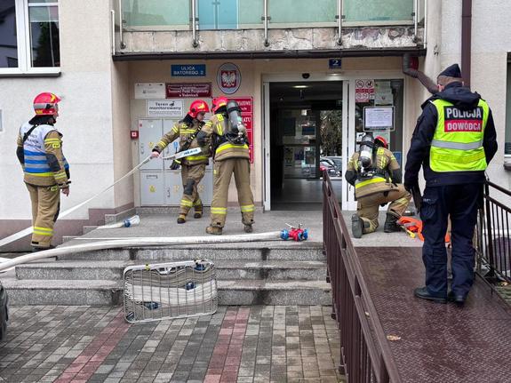 Przed budynkiem Starostwa Powiatowego czterech strażaków oraz policjant.